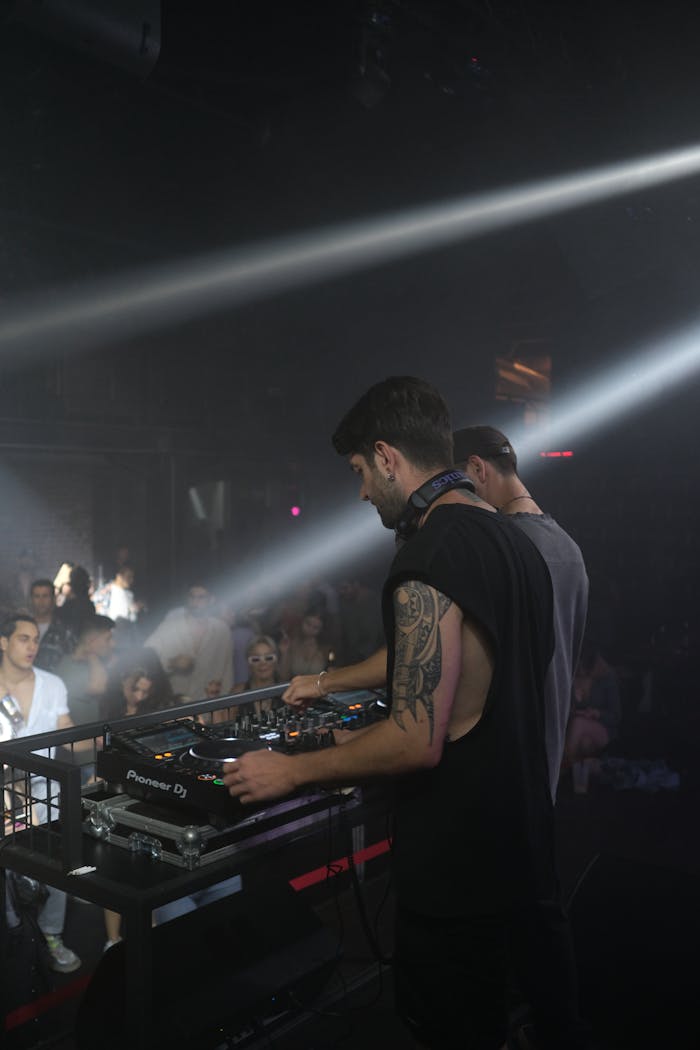 DJ playing live in a nightclub with a colorful audience and stage lighting.